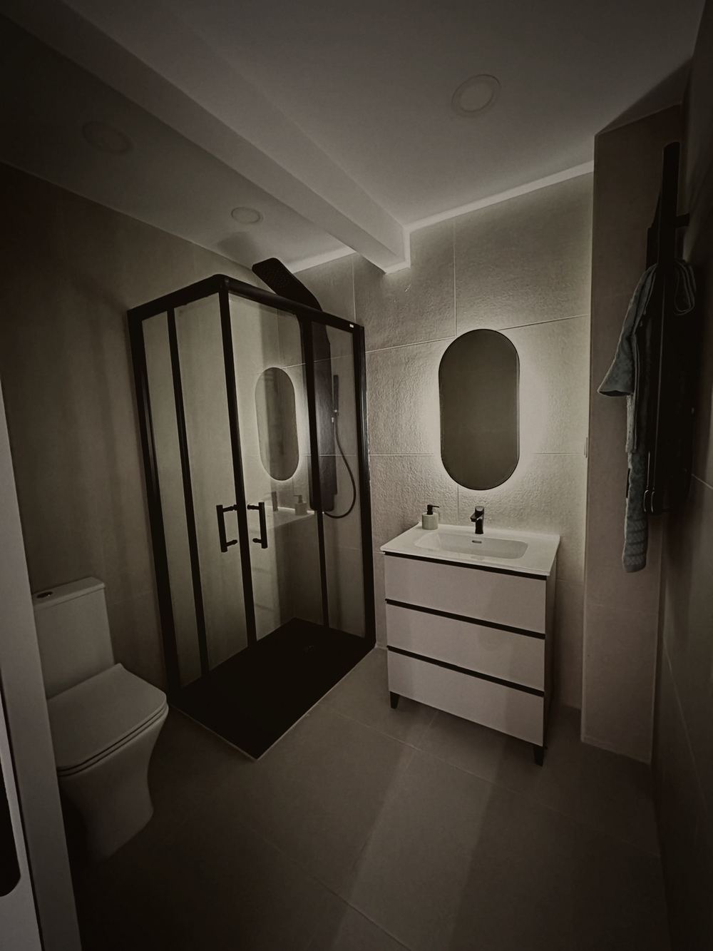 Baño reformado: mampara negra a medida, espejo retroiluminado, mueble suspendido y luz indirecta perimetral